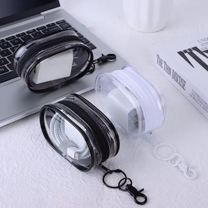 May include: Two oval-shaped, transparent storage pouches with zipper closures and attached metal key ring clips. One pouch features a black zipper and trim, while the other has a white zipper and trim. Both contain white power adapters and cables.
