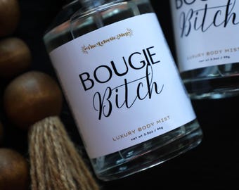 May include: Clear glass body mist bottles with white labels featuring the text "BOUGIE Bitch" in black script. The labels also include "The Eclectic Meg" and "LUXURY BODY MIST". The net weight is 3.5oz / 99g.