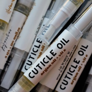 May include: A close-up of several white and clear plastic bottles with labels that read "Cuticle Oil" and "argan oil + vit e".