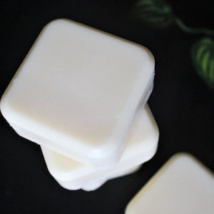 May include: Three white square-shaped bars of soap stacked on top of each other on a black surface.
