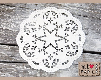 May include: White paper doily with a delicate, intricate design. The doily is circular and has a scalloped edge. It is on a rustic wooden background. The text "mit & papier" is visible in the lower right corner.