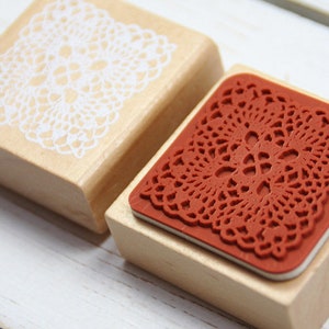 May include: Two wooden stamps with intricate lace designs. One stamp features a white lace design on a natural wood block, while the other has a red lace design on a wood block.