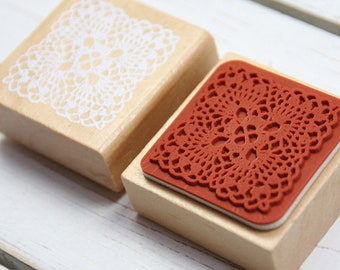 May include: Two wooden stamps with intricate lace designs. One stamp features a white lace design on a natural wood block, while the other has a red lace design on a wood block.