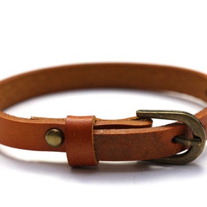 Könnte beinhalten: Ein braunes Lederarmband mit einer Metallschnalle. Das Armband ist schlicht und elegant.