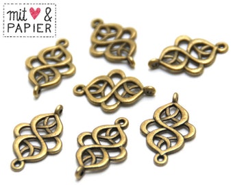 May include: Close-up of several antique brass-colored filigree charms. Each charm features an intricate, openwork design with a loop at the top and bottom for attaching to other components. The charms are arranged on a white background. The text "mit & PAPIER" is in the upper left corner.