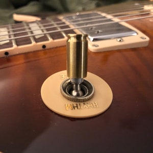 May include: A close-up of a gold-coloured guitar toggle switch with a brass bullet-shaped knob. The switch is labelled "RHYTHM" in gold lettering.