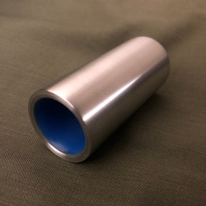 May include: A cylindrical metal guitar slide with a polished silver exterior and a bright blue interior. The slide is made of a solid material and is designed to be worn on a finger for playing a guitar.