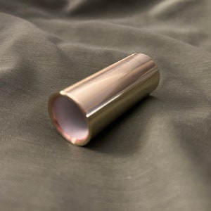 May include: A gold-colored metal guitar slide, a device used to create a smooth, sustained sound on a guitar.