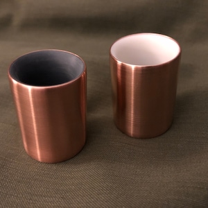May include: Two copper mugs with a brushed finish. One mug has a black interior and the other has a white interior.
