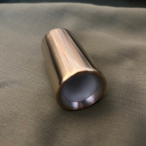 Könnte beinhalten: Ein glänzendes, silberfarbenes Metallrohr mit einer glatten, abgerundeten Oberfläche. Das Rohr hat einen leicht dunkleren, fast kupferfarbenen Rand um die Öffnung.