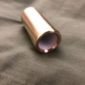 May include: A gold-colored metal slide for a guitar, with a white interior.