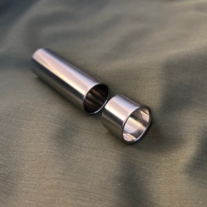 May include: Two silver metal slide guitar slides, one is a tube shape and the other is a ring shape.