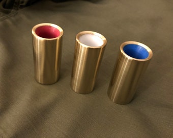 Può includere: Tre slide per chitarra slide in metallo color oro con inserti di diversi colori. Lo slide a sinistra ha un inserto rosso, lo slide centrale ha un inserto bianco e lo slide a destra ha un inserto blu.