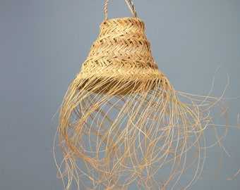 May include: A natural woven lampshade with a fringe of long, thin strands hanging down. The lampshade is made of a light brown material and has a conical shape.