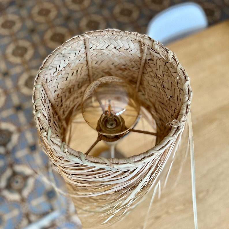 May include: A woven lampshade made of natural materials, with a light bulb inside. The lampshade is beige and has a natural, rustic look.
