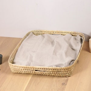 Op de afbeelding: Een rechthoekige geweven mand met een lichtbruine stoffen voering. De mand is gemaakt van natuurlijke materialen en heeft een rustieke uitstraling.