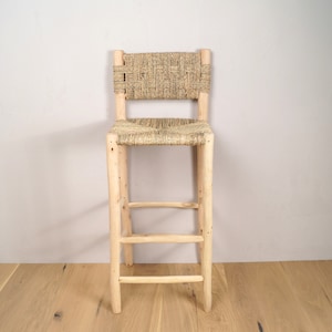 May include: A wooden bar stool with a woven straw seat and back. The stool has a simple design with three horizontal supports.