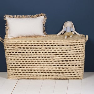 Peut inclure: Un panier de rangement en jonc de mer tress&eacute; avec un coussin blanc et un petit lapin en peluche sur le dessus. Le panier a deux poign&eacute;es et est de couleur beige naturel.