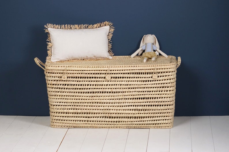 Peut inclure: Un panier de rangement en jonc de mer tress&eacute; avec un coussin blanc et un petit lapin en peluche sur le dessus. Le panier a deux poign&eacute;es et est de couleur beige naturel.