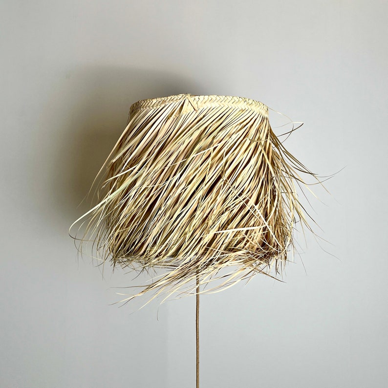 May include: A natural woven lampshade made of straw with a fringed edge. The lampshade is beige and has a natural, rustic look.