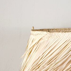 May include: A large, natural woven lampshade made of dried palm leaves. The shade is light brown and has a fringed edge.