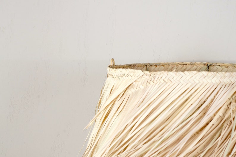 May include: A large, natural woven lampshade made of dried palm leaves. The shade is light brown and has a fringed edge.