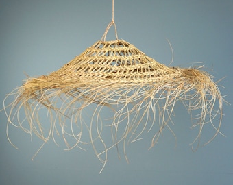 May include: A woven straw lampshade with a fringe of natural fibers hanging from the bottom. The lampshade is light brown and has a natural, rustic look.