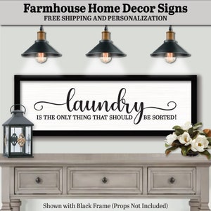 May include: A black framed sign with white background and black calligraphy that reads "laundry is the only thing that should be sorted!" The sign is hanging on a wall above a gray wooden dresser with three drawers. There are three black pendant lights hanging above the sign.