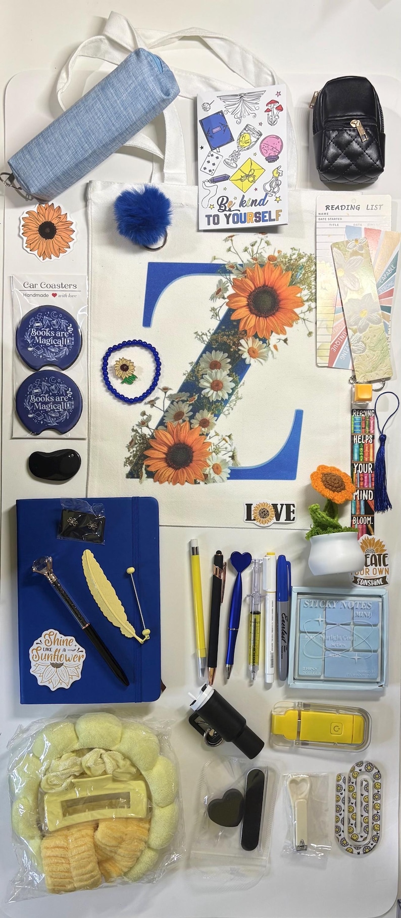 May include: A collection of stationery and accessories including a floral letter Z tote bag, a blue notebook with a sunflower sticker, various pens, a small potted crochet sunflower, sticky notes, car coasters, bookmarks, and a small black quilted bag.