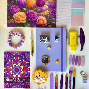 May include: A collection of purple and yellow stationery items including a floral notebook, a daily planner, a Mindful Patterns coloring book, a purple journal, pens, a pencil case, a crochet sunflower, a sleep mask, and various small accessories.