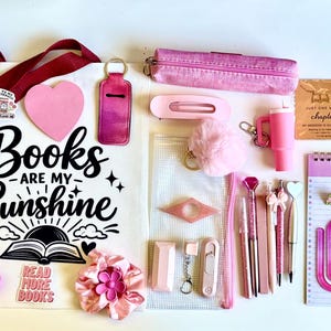 May include: A collection of pink-themed stationery and accessories including a tote bag with the text Books Are My Sunshine, a daily planner, a notebook, pens, a pencil case, bookmarks, a hair clip, a keychain, and various small decorative items.