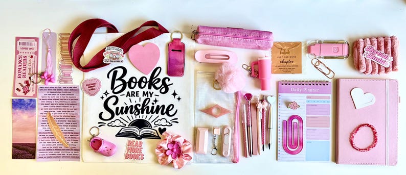 May include: A collection of pink-themed stationery and accessories including a tote bag with the text Books Are My Sunshine, a daily planner, a notebook, pens, a pencil case, bookmarks, a hair clip, a keychain, and various small decorative items.