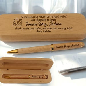 Könnte beinhalten: Ein helles Holz-Stifteetui mit einer eingravierten Nachricht über einen Architekten, neben einem passenden Holzstift mit goldenen Akzenten. Ein zweites offenes Holz-Stifteetui enthält einen identischen Stift mit der Gravur Roxanne Berry, Architect.