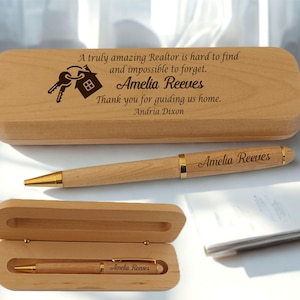 May include: A light brown wooden pen and case set. The pen has gold detailing and the name "Amelia Reeves" engraved. The case has a message and a key and house graphic. The set is a gift for a realtor.