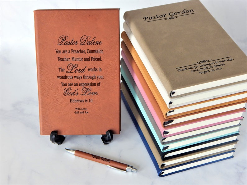 K&ouml;nnte beinhalten: Ein Stapel brauner Lederjournale mit personalisierten Gravuren. Das oberste Journal tr&auml;gt den Text "Pastor Gordon" und das unterste Journal den Text "Pastor Dalene". Die Journale befinden sich auf einer wei&szlig;en Oberfl&auml;che.