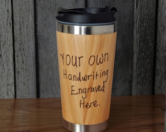 May include: A bamboo travel tumbler with a black plastic lid and a stainless steel base. The exterior features the laser-engraved text: Your own Handwriting Engraved Here. The cup has a tapered cylindrical shape with a light wood grain finish.