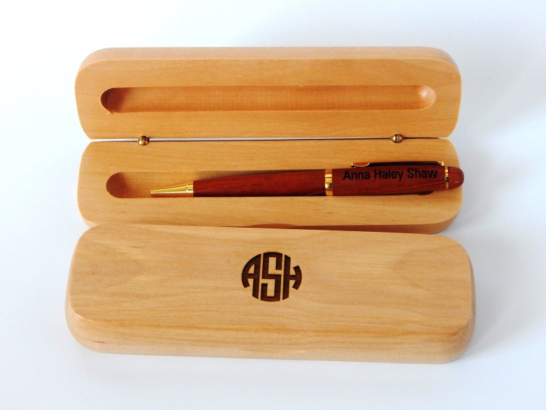 May include: A wooden pen box with a brown pen inside. The pen has gold accents and is engraved with the name "Anna Haley Shaw". The box is also engraved with the initials "ASH".