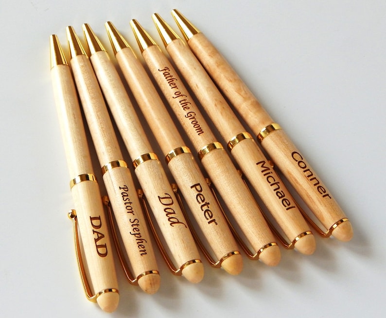 May include: Seven wooden pens with gold accents and personalized engravings. The engravings include "Dad", "Pastor Stephen", "DAD", "Peter", "Father of the Groom", "Michael", and "Conner".