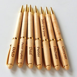 May include: Seven wooden pens with gold accents and engraved names. The pens are light brown with gold tips and clips. The engraved names include "DAD", "Pastor Stephen", "Dad", "Peter", "Father of the Groom", "Michael", and "Conner".