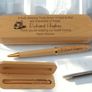 Puede incluir: Un juego de pluma y estuche de madera. La pluma es de color marrón claro con detalles dorados y el nombre "Richard Hughes" grabado. El estuche también es de color marrón claro y tiene el mismo nombre grabado, junto con un mensaje y un gráfico de camión.