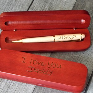 May include: A wooden pen and case set. The pen is light-colored with gold accents and the words "I love you" engraved on the barrel. The case is a deep red-brown color, with "I Love You Daddy" engraved on the lid.