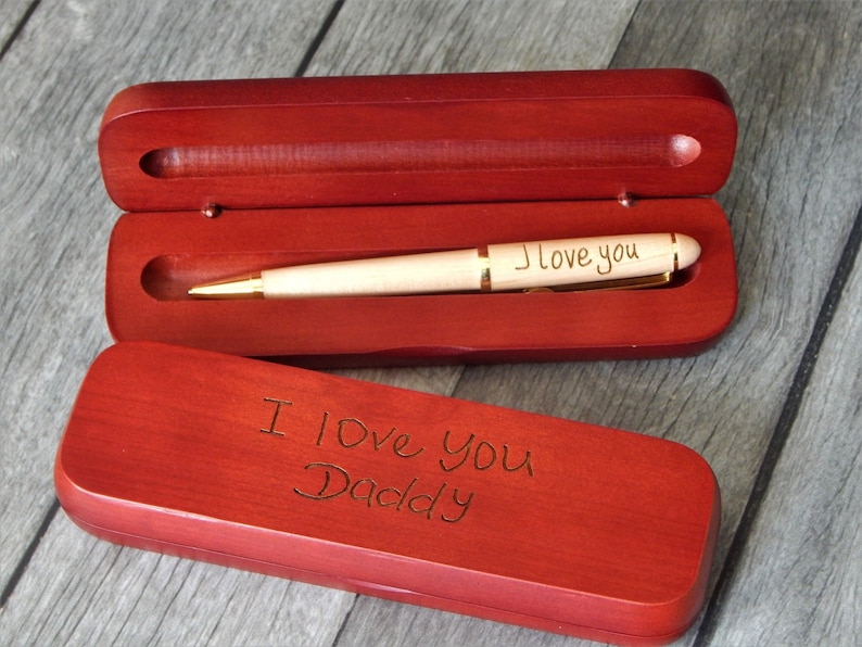 May include: A wooden pen and case set. The pen is light-colored with gold accents and the words "I love you" engraved on the barrel. The case is a deep red-brown color, with "I Love You Daddy" engraved on the lid.