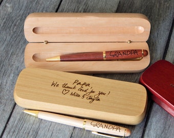 May include: A dark wood pen engraved with the word GRANDPA resting in an open light wood case. A second light wood pen engraved with GRANDPA lies next to a closed light wood case engraved with Papa, We thank God for you! Mille & Jayla.