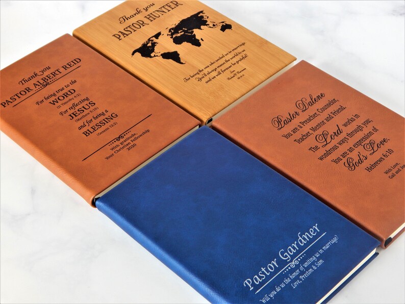 K&ouml;nnte beinhalten: Vier verschiedene ledergebundene Notizb&uuml;cher mit personalisierten Gravuren. Jedes Notizbuch hat eine andere Farbe und ein anderes Design, darunter eine Weltkarte, ein Zitat &uuml;ber den Glauben und eine Botschaft zum Thema Hochzeit. Die Notizb&uuml;cher sind ideal f&uuml;r Geschenke oder die pers&ouml;nliche Verwendung.