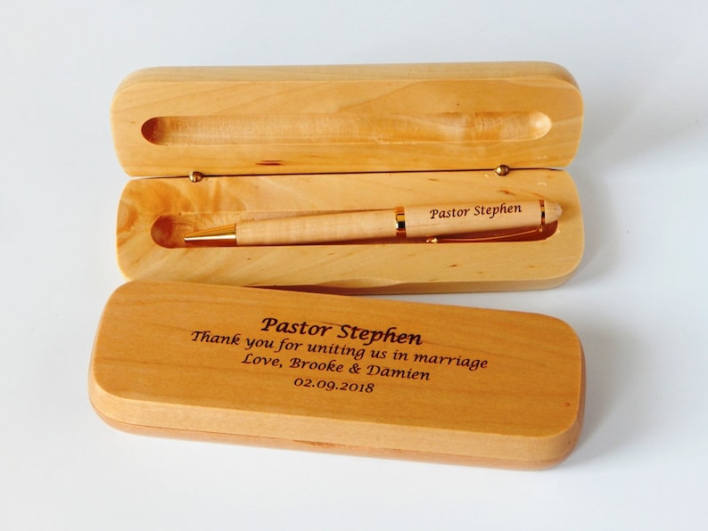 May include: A wooden pen box with a pen inside. The box is engraved with the text "Pastor Stephen Thank you for uniting us in marriage Love, Brooke & Damien 02.09.2018".