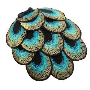 May include: A black felt hair clip with a peacock feather design. The feathers are embroidered with gold and blue thread.