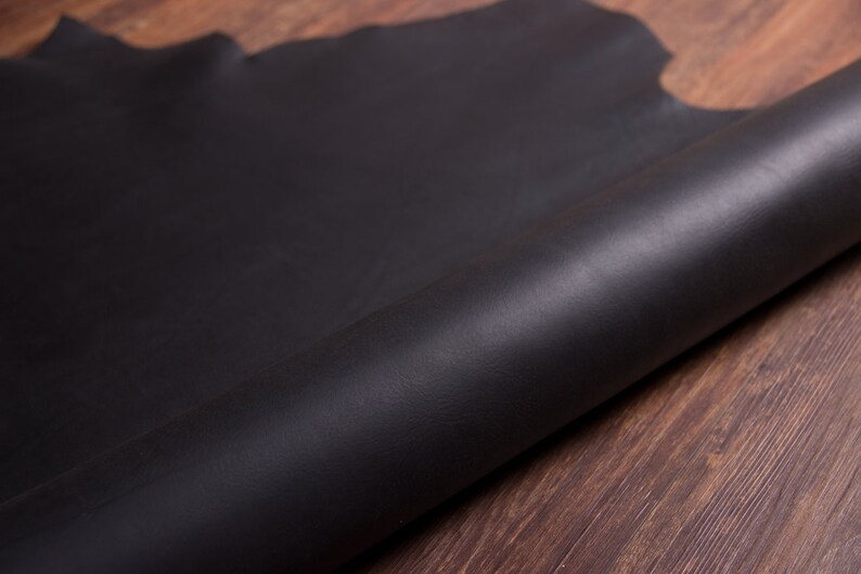 May include: A close-up of a black leather sheet rolled up on a wooden surface.