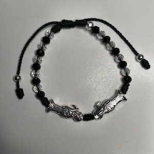 May include: Black and clear beaded bracelet with silver-toned charms. The bracelet features a series of black and clear beads, with two silver charms. The bracelet is adjustable with black cords and silver bead accents.