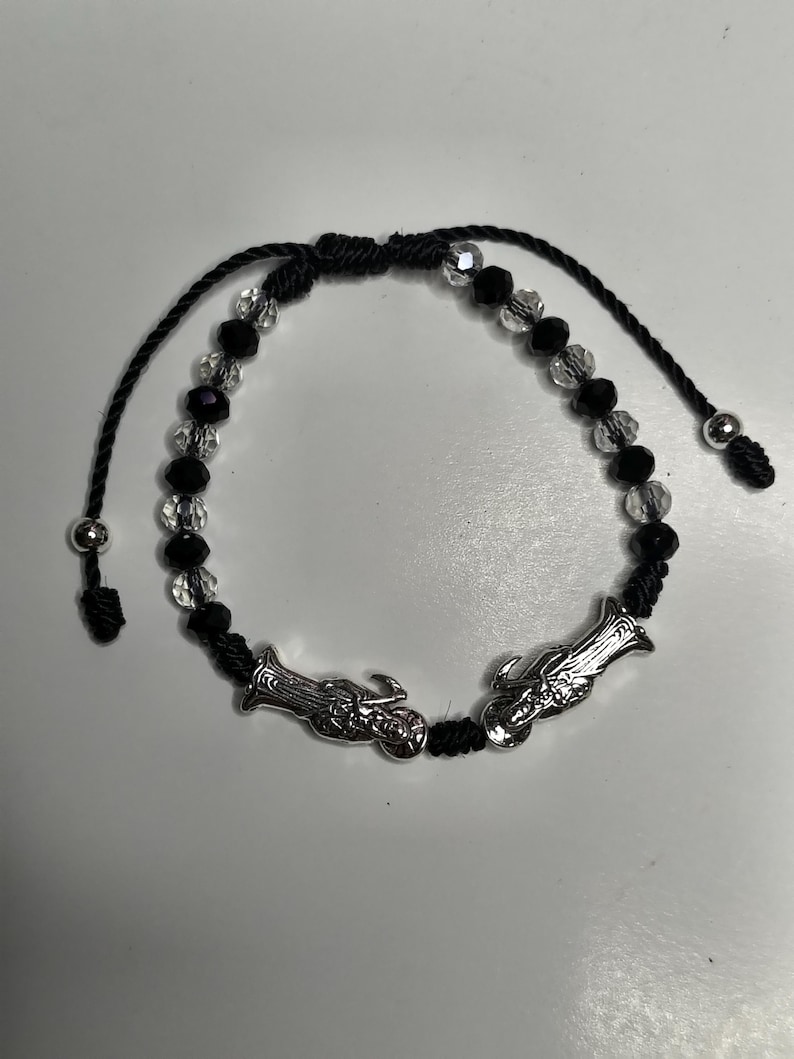 May include: Black and clear beaded bracelet with silver-toned charms. The bracelet features a series of black and clear beads, with two silver charms. The bracelet is adjustable with black cords and silver bead accents.