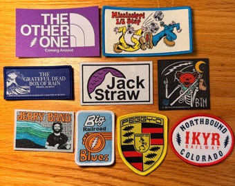 May include: A collection of embroidered patches with various designs and text. Patches include "The Other One," "Mississippi 1/2 Step," "The Grateful Dead Box of Rain," "Jack Straw," "Jerry Band," "Big Railroad Blues," "Peggy-O," and "Northbound IKYR Railway Colorado."